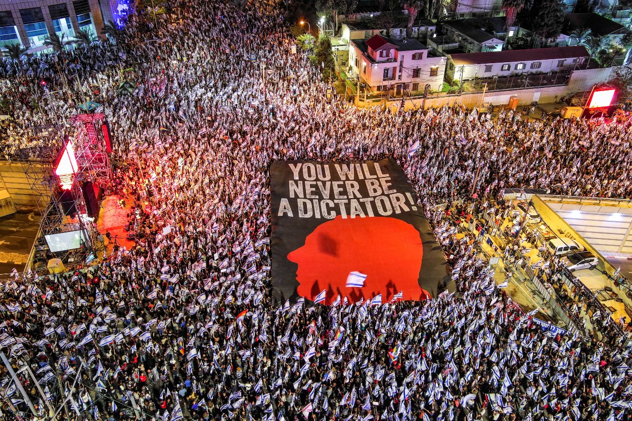 Davy ľudí, ktorí sa zišli na protestoch a banner s nápisom proti premiérovi Netanjahuaovi "You will never be a dictator!", v preklade "Ty nikdy nebudeš diktátor!" 