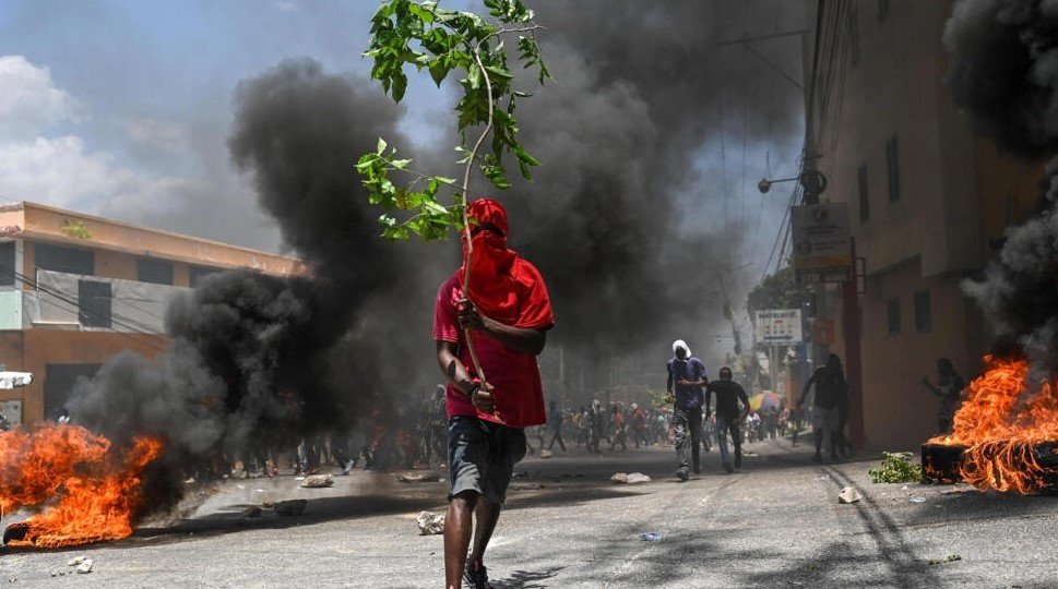 Muž drží vetvu stromu a pochoduje pri pálení pneumatík počas protestu proti neistote 7. augusta 2023 neďaleko úradného domu premiéra v Port-au-Prince na Haiti.