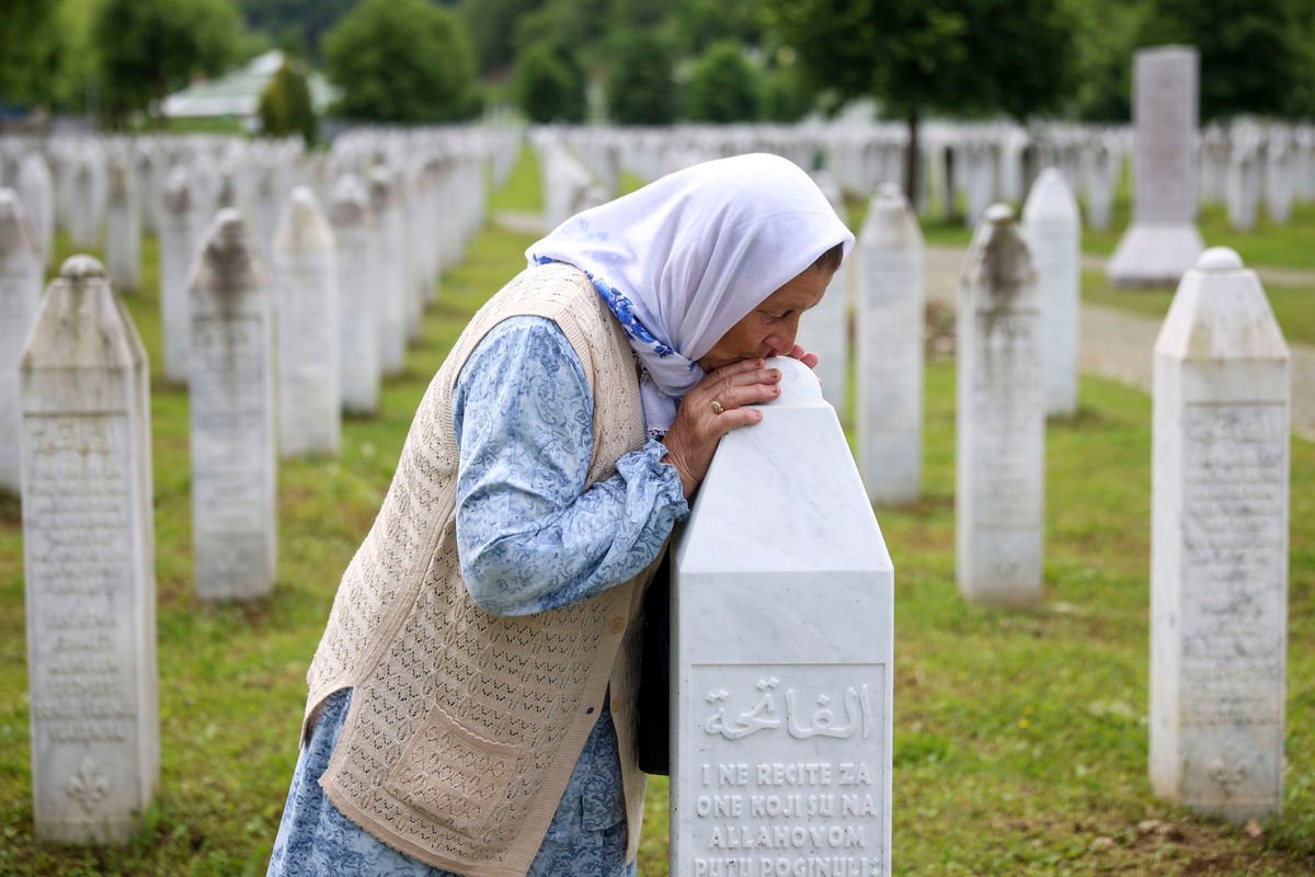 Žena bozkáva hrob svojho syna, ktorý sa stal obeťou genocídy v Srebrenici, na pamätnom cintoríne v Potočari na východe Bosny v stredu 22. mája 2024.