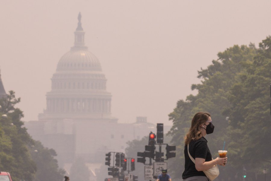 Ilustračné foto - chodkyňa s respiračnou maskou na tvári vo Washingtone, D.C., USA, 29. júna 2023 pri budove Kapitolu USA zahalenou v smogu.