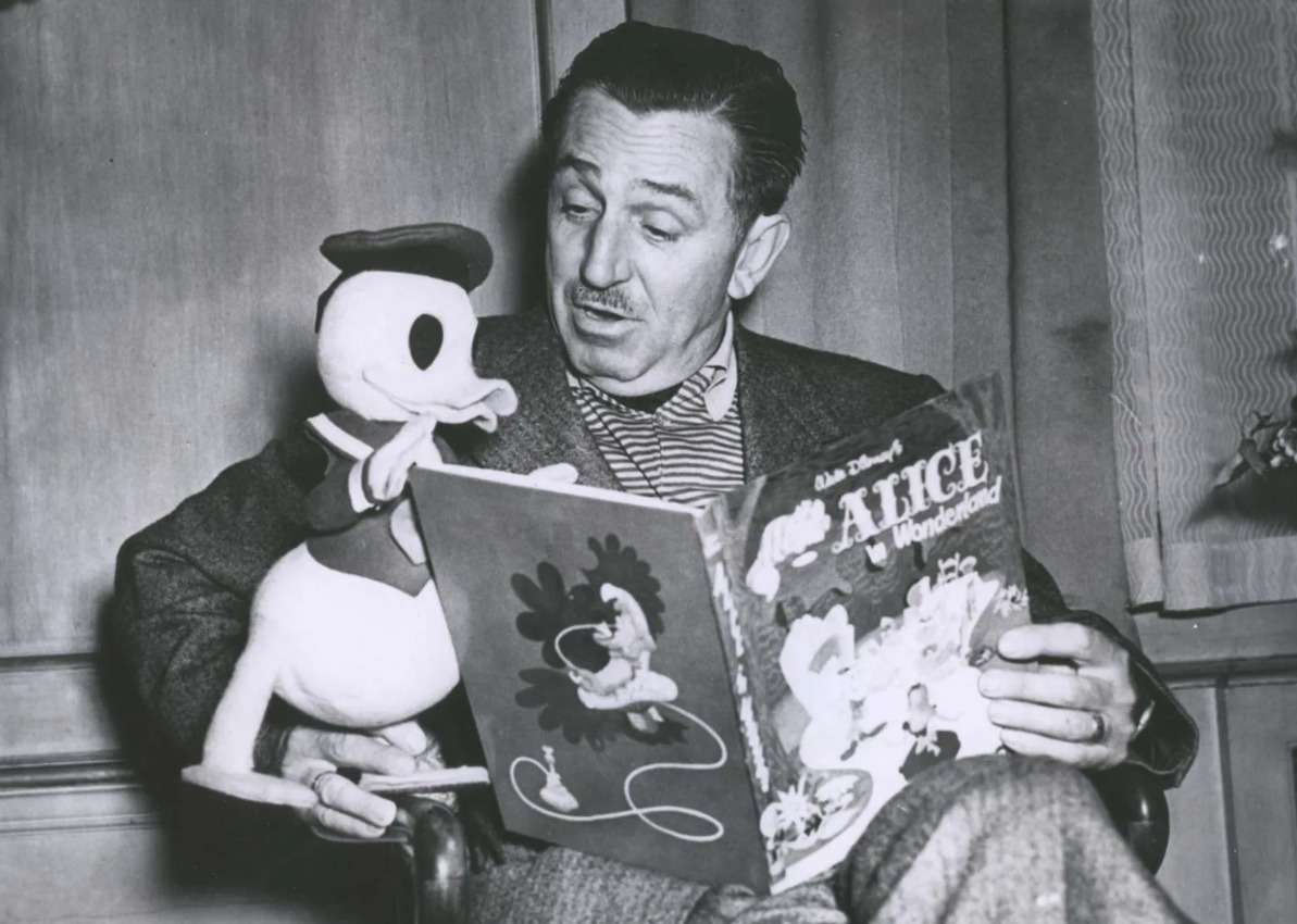 Ilustračné foto - Walt Disney predstiera, že číta Alicu v krajine zázrakov vypchatej postavičke káčera Donalda, 1954.