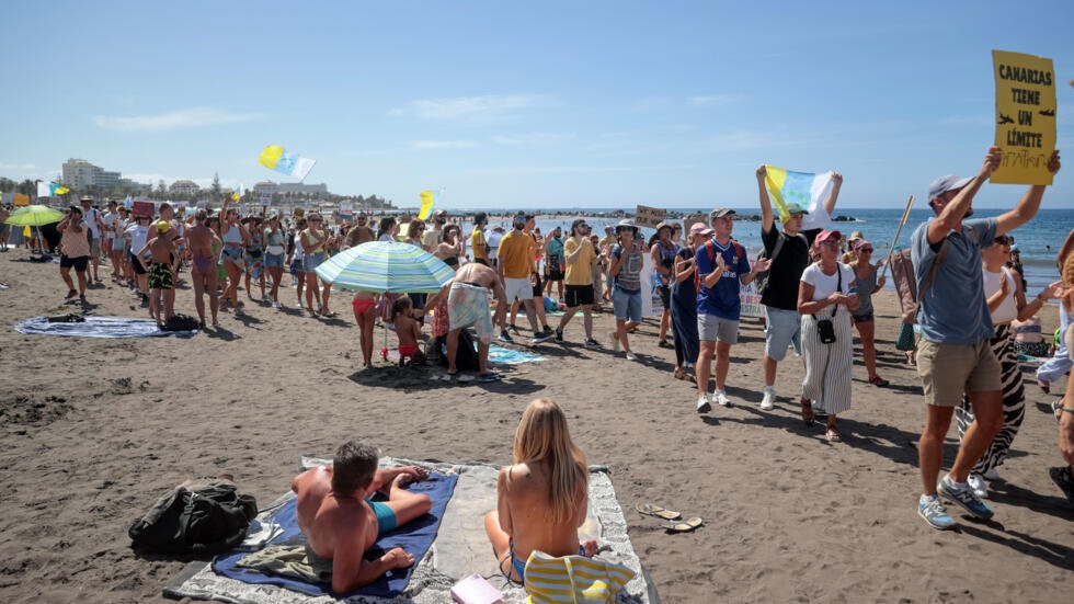 Mávajúci bielymi, modrými a žltými vlajkami Kanárskych ostrovov, skandujúci a pískajúci demonštranti pomaly prechádzali okolo turistov sediacich na vonkajších terasách v Playa de las America na Tenerife predtým, ako sa zhromaždili na pláži.